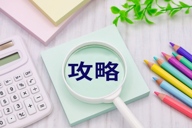 虫眼鏡に映る「攻略」の文字・色鉛筆・電卓が並ぶ攻略Tips用イメージ写真