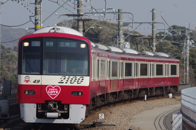 快特三崎口行きの赤い京急電車(KEIKYU LOVE TRAINラッピング)が線路を走る様子