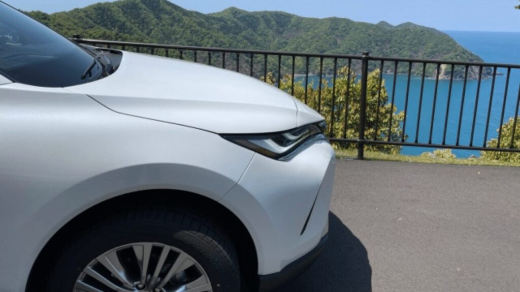 海沿いの展望スポットに停まる白い車と青い海の風景