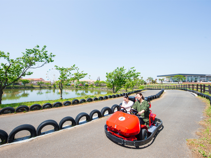 ソレイユの丘のゴーカート|赤いカートに乗る2人と池のある園内風景