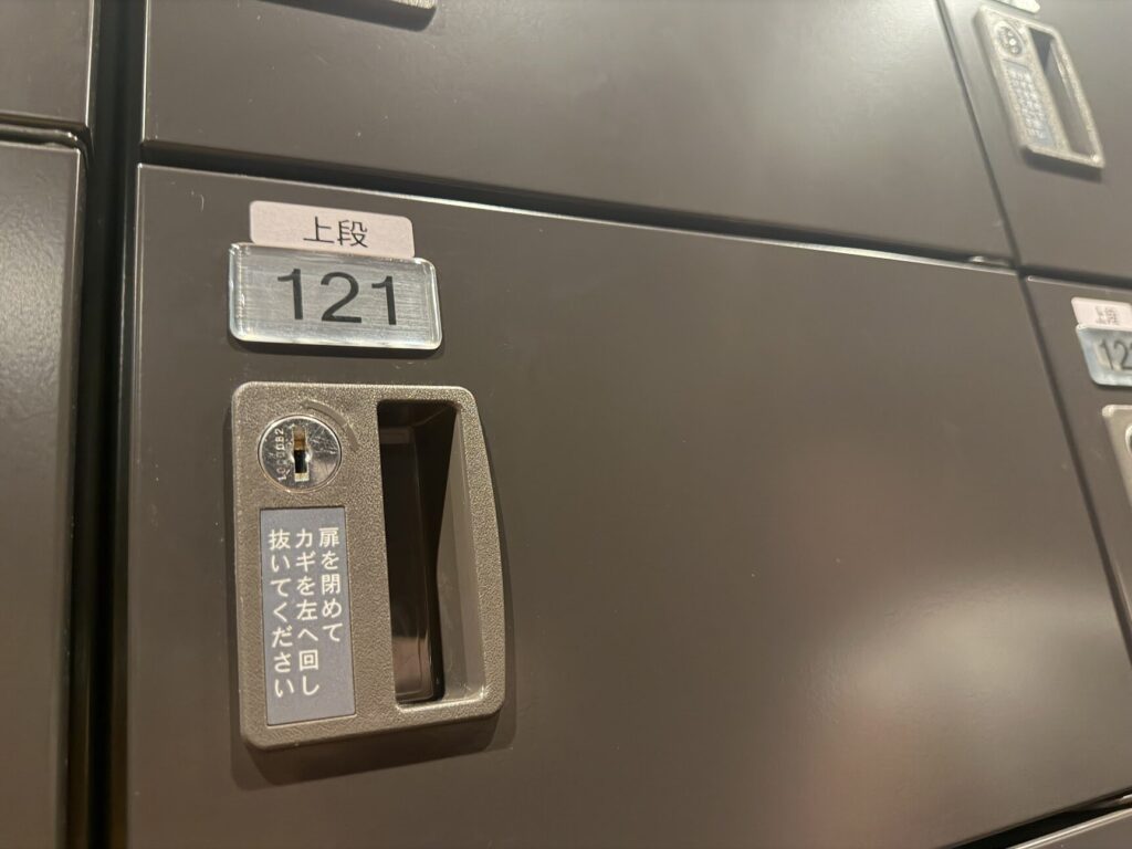 下駄箱の鍵部分のクローズアップ（「上段121」の番号プレートと「扉を閉めてカギを抜いて左にまわしてください」の案内）