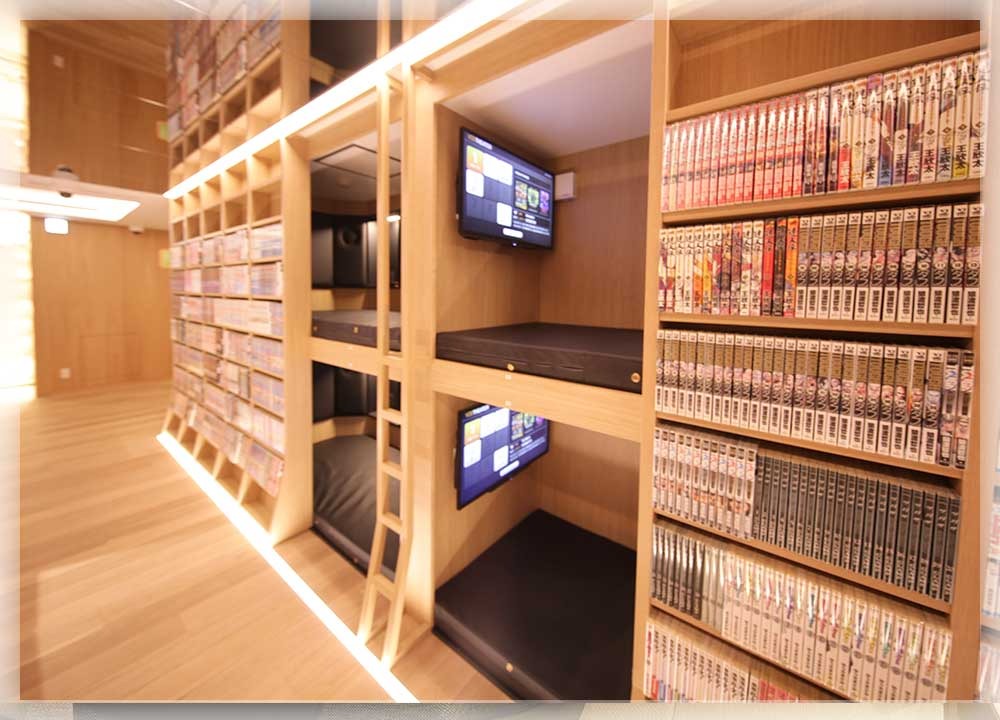 木製の棚に囲まれた半個室ブースが上下2段に並ぶ。各ブースにTV画面が設置され、周囲の棚にはカラフルな漫画がびっしり並んでいる。温かみのある間接照明の空間