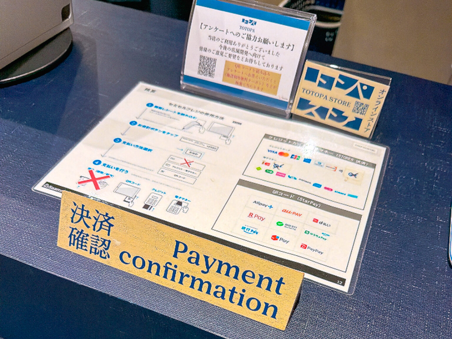 受付カウンターに置かれた「決済確認 Payment confirmation」の案内カード。対応するキャッシュレス決済のロゴが並び、現金には×印が付けられている