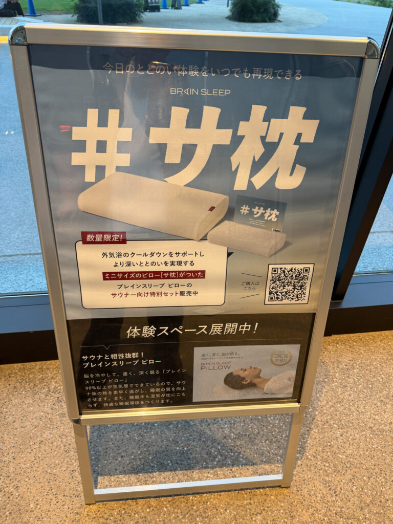「#サ枕(サウナ枕)」のレンタル案内サイン。木製のサウナ枕のサンプルとQRコードが添えられ、体験スペース展開中と書かれている