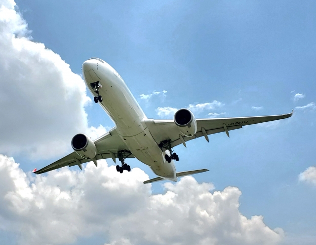 青空と白い雲を背景に、着陸脚を出して飛ぶ白い旅客機