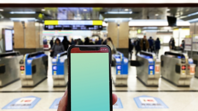 駅の自動改札機の前でスマートフォンを持つ様子