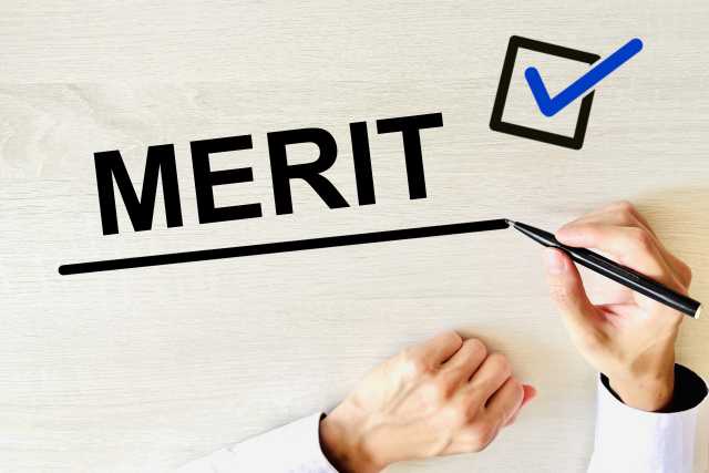木目のテーブルの上で「MERIT」の文字に下線を引く手と、青いチェックマークが入ったチェックボックス