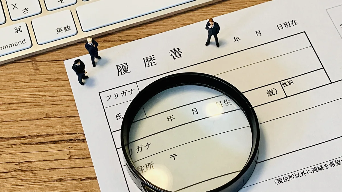 履歴書と虫眼鏡でリゾートバイトの求人条件を細かく確認するイメージ