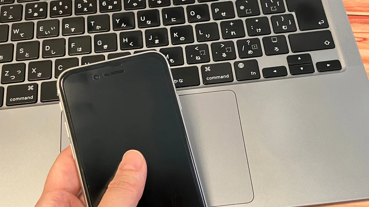 ノートパソコンの前でスマートフォンを操作する手元