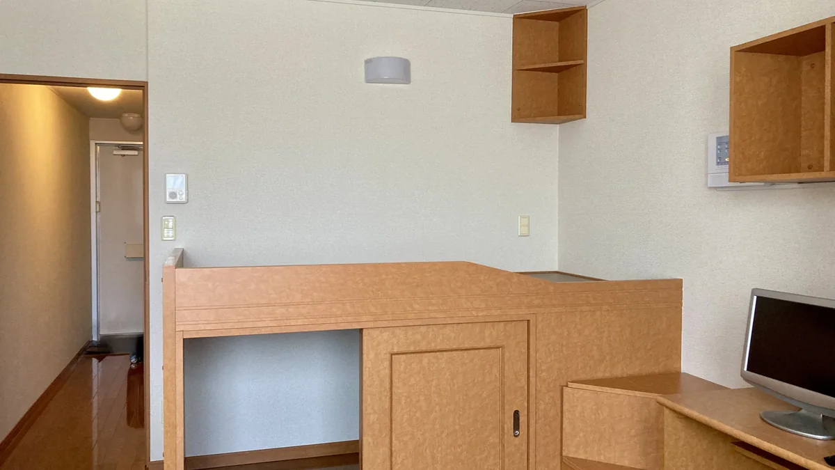 ベッドと机と収納がある一人用の部屋で個室寮の設備を確認するイメージ