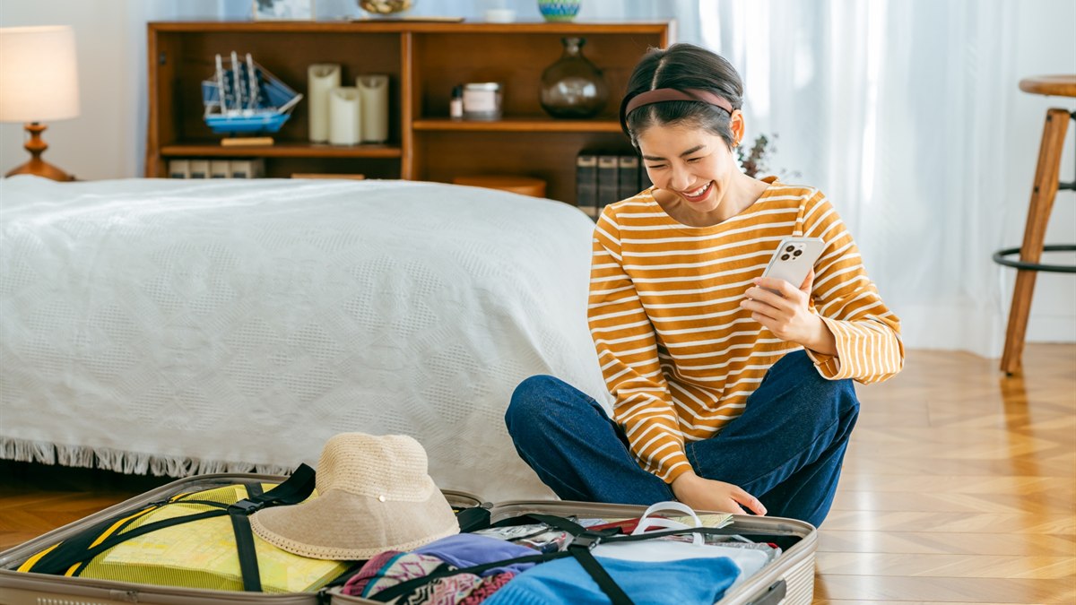 旅行前にスマートフォンで予約内容を確認する女性とスーツケース