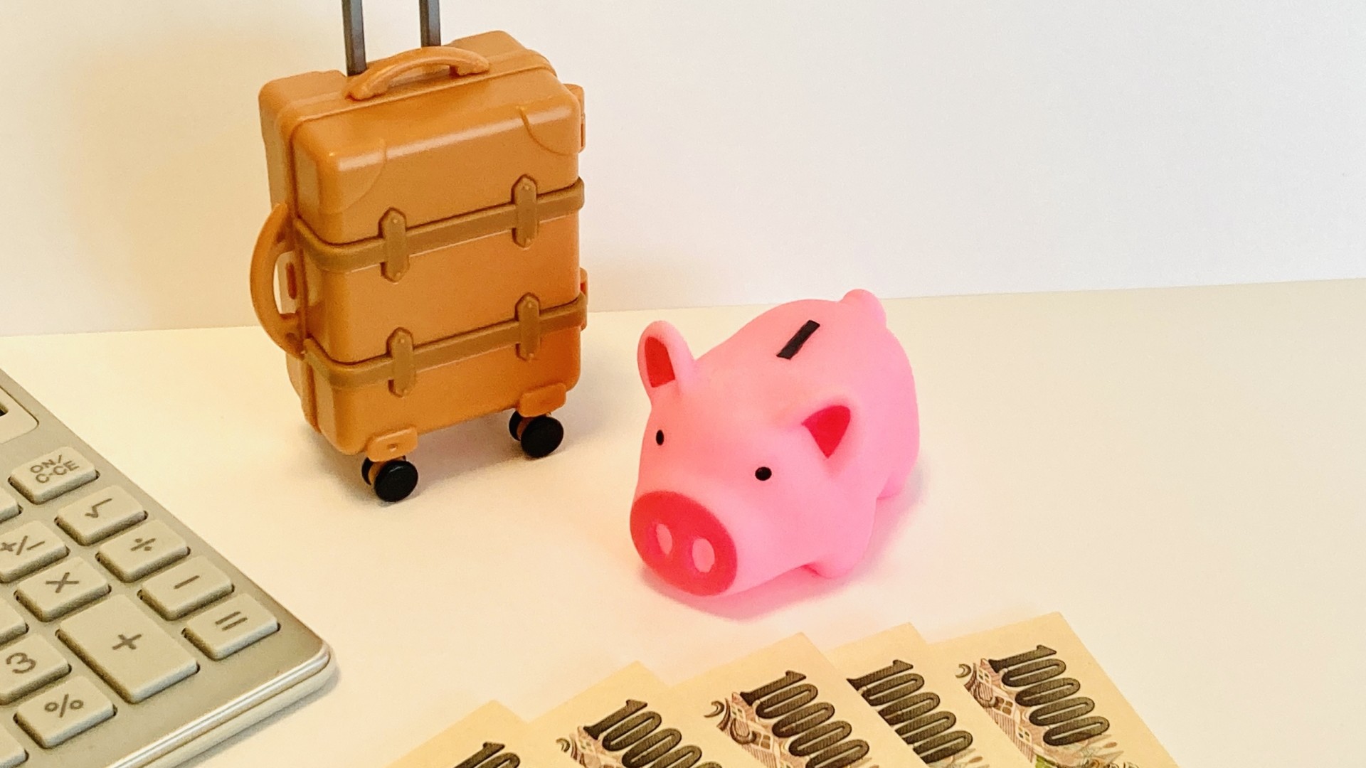 スーツケースと貯金箱と電卓で旅行費用を比べるイメージ
