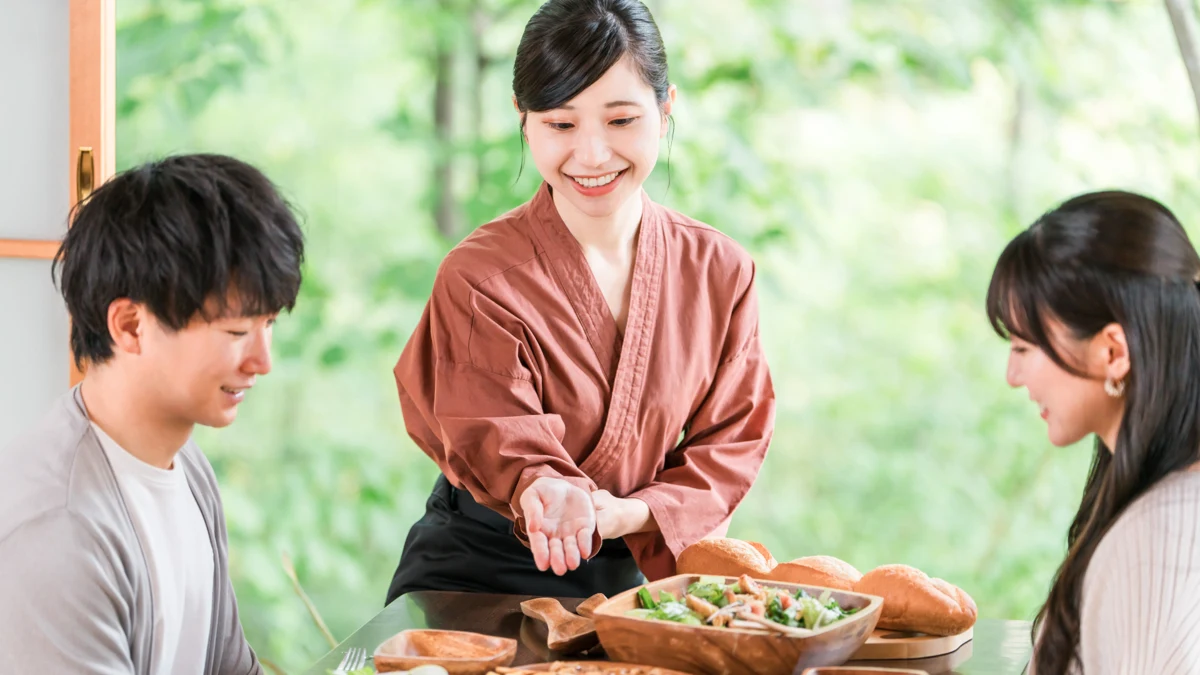 旅館で食事中の宿泊客に料理を説明する接客スタッフのイメージ