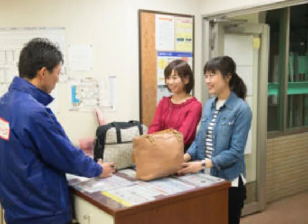 箱根キャリーサービスの受付カウンターでスタッフに荷物を預ける旅行者